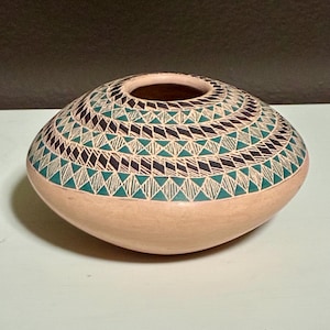 May include: A hand-painted ceramic pot with a rounded base and a wide opening. The pot features a geometric pattern of teal, black, and white diamonds and triangles on a light peach background. The pottery is likely handmade and suitable for home decor.