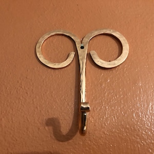May include: A gold metal hook with two loops at the top. The hook is hammered and has a textured finish.