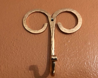 May include: A gold metal hook with two loops at the top. The hook is hammered and has a textured finish.
