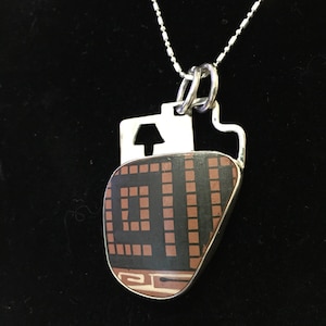 May include: A silver chain necklace with a pendant featuring a geometric design in black, brown, and white on a stone. The pendant is shaped like a heart.