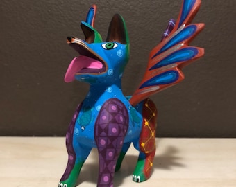 May include: A colorful wooden figurine of a dog with wings. The dog is painted in shades of blue, green, purple, red, and yellow. The wings are painted in shades of blue, red, and silver. The dog has a long tongue sticking out and a playful expression.