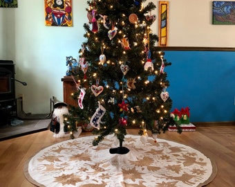 Pode incluir: Uma saia de árvore de Natal branca com um padrão floral castanho. A saia é colocada num chão de madeira debaixo de uma árvore de Natal decorada.