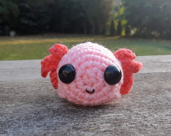 May include: A pink crocheted axolotl plushie with large black eyes and red crocheted gills.