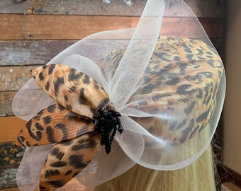 May include: A white mesh hat with a leopard print fabric bow and a black beaded embellishment.