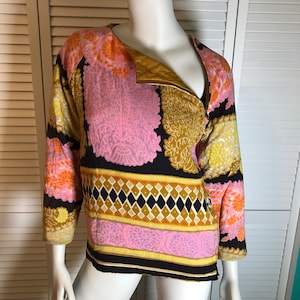 Könnte beinhalten: Eine schwarze, rosa, gelbe und orangefarbene gemusterte Jacke mit Reißverschluss. Die Jacke hat ein geometrisches Muster am unteren Rand.