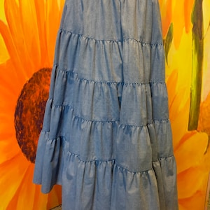 May include: A light blue denim skirt with multiple tiers. The skirt has a wide elastic waistband and falls to the lower calf.