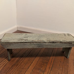 May include: A small, rustic wooden bench with a weathered, light blue paint finish. The bench has a simple design with two legs on each end.