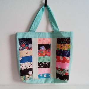 May include: A light blue tote bag with a patchwork design. The bag is made of different fabrics with various patterns, including flowers, music notes, stars, and geometric shapes.
