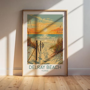 May include: Framed art print of Delray Beach, Florida, featuring a sunset over the ocean. The artwork depicts a sandy path leading to the beach, framed by tall grass and a wooden fence. The sky transitions from orange to blue.