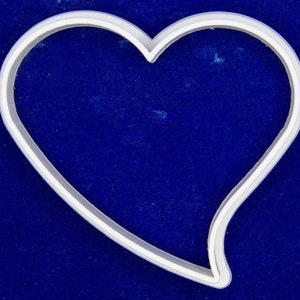 May include: A silver-colored heart-shaped cookie cutter. The cutter has a smooth, rounded design with a defined outline. The heart shape is open, with a small indentation at the top center.