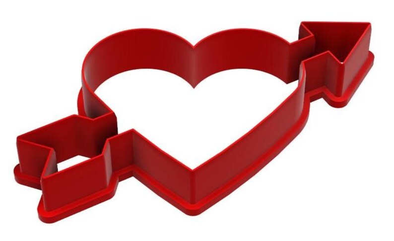 May include: A red plastic cookie cutter in the shape of a heart pierced by an arrow. The arrow's fletching and arrowhead are clearly defined. The cutter is designed for baking and crafting, perfect for Valentine's Day or other romantic occasions.