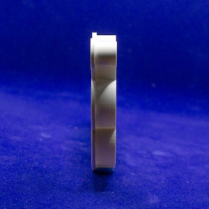 May include: A white, vertically oriented object with a layered design, possibly a cookie cutter or a similar craft tool. The object is set against a deep blue background, creating a contrast that highlights its shape and texture. The object appears to be made of a rigid material.