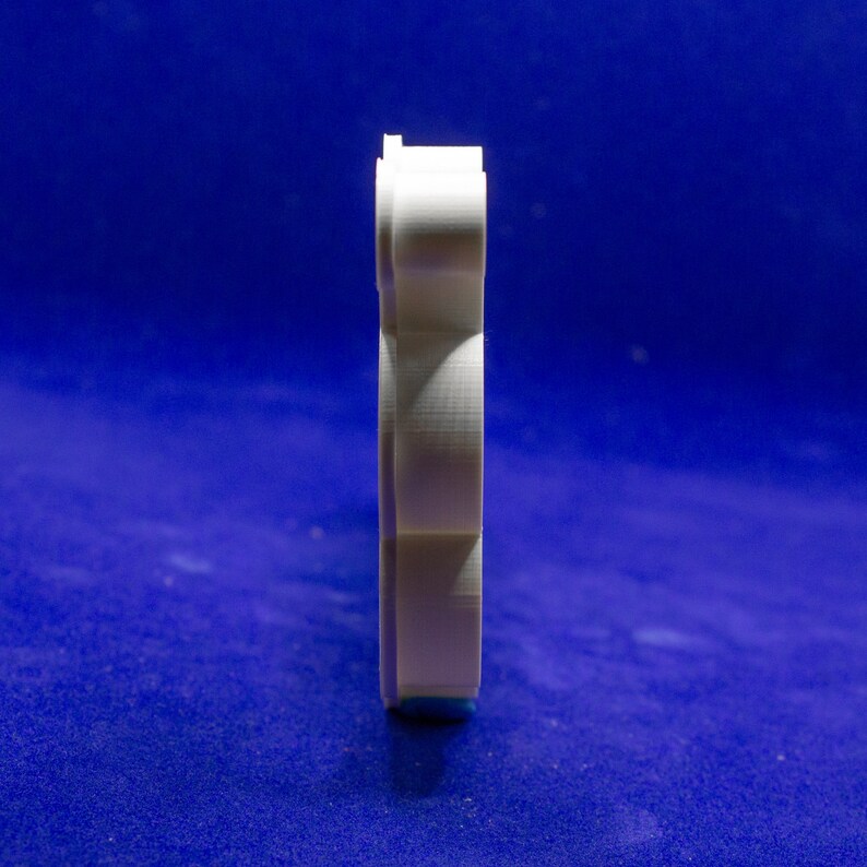 May include: A white, vertically oriented object with a layered design, possibly a cookie cutter or a similar craft tool. The object is set against a deep blue background, creating a contrast that highlights its shape and texture. The object appears to be made of a rigid material.