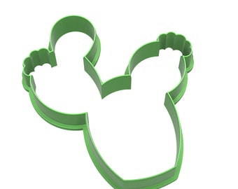 May include: A green plastic cactus-shaped cookie cutter. The cutter features a simple outline with two rounded sections at the top and a wider base. The edges are smooth, and the design is clean and modern.