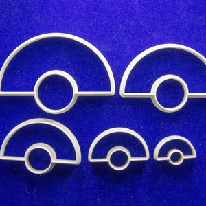 May include: A collection of white plastic cookie cutters in various sizes, each featuring a semi-circular top and a circular base. The cutters are arranged on a blue surface, showcasing their different dimensions.