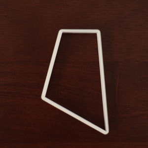 May include: A white, trapezoid-shaped object with a thin, rectangular profile. The object is positioned on a dark brown wooden surface. The shape is a four-sided polygon with two parallel sides and two non-parallel sides.