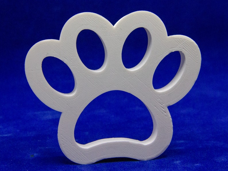 May include: A white, three-dimensional paw print cutout. The paw print has four oval toe pads and a larger, rounded heel pad. The object is made of a solid, textured material and is set against a blue background.