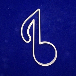 May include: A white plastic cookie cutter in the shape of a musical eighth note. The cutter has a curved top and a circular bottom, with a straight line connecting them. The cutter is set against a dark blue background.