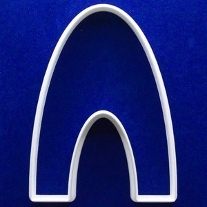 Puede incluir: Cortador de galletas de plástico blanco en forma de arco, con un arco más pequeño en el interior. El cortador está sobre un fondo azul liso. El diseño es simple y limpio, adecuado para hornear.
