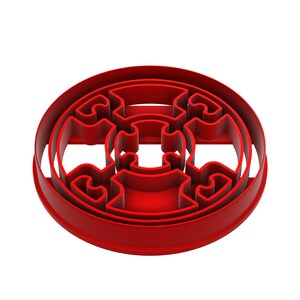 May include: A red, circular cookie cutter with an intricate, symmetrical design. The cutter features a series of interconnected shapes within a rounded border, perfect for creating detailed cookies or pastries. The design is raised, creating a defined edge for cutting.