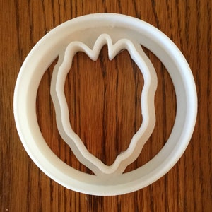 May include: A white plastic cookie cutter with a circular outer ring and a stylized leaf shape inside. The cutter is designed for creating cookies or other baked goods with a unique botanical design.