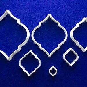 Puede incluir: Un juego de seis cortadores de galletas de plástico blanco con diseño de azulejo marroquí. Los cortadores son de varios tamaños, con una forma arqueada repetida, sobre un fondo azul.