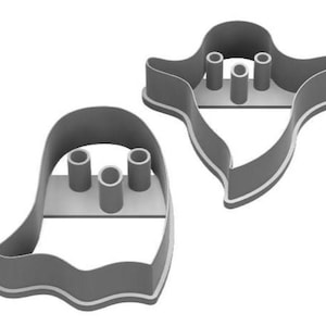May include: Two gray ghost-shaped cookie cutters. Each cutter has a rounded top, a wavy bottom, and three cylindrical supports. The edges are outlined in white. These cutters are ideal for Halloween-themed baking.