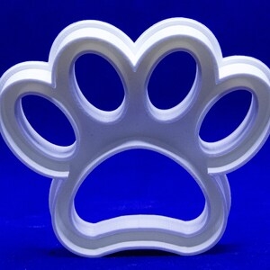 May include: A white, three-dimensional paw print cookie cutter. The cutter is made of a light-colored plastic and has a layered design. The background is a solid, deep blue.