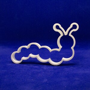 May include: A white plastic caterpillar-shaped cookie cutter. The cutter has a segmented body and a rounded head with antennae. The design is simple and clean, perfect for creating fun treats.