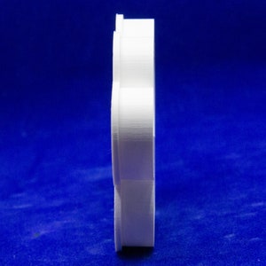 May include: A side view of a white, 3D-printed object with a layered, curved design. The object is set against a deep blue background. The shape appears to be a stylized, abstract form.