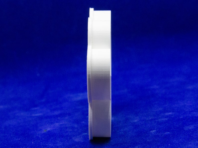 May include: A side view of a white, 3D-printed object with a layered, curved design. The object is set against a deep blue background. The shape appears to be a stylized, abstract form.