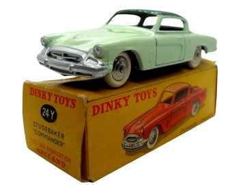 May include: A green Studebaker Commander toy car in a yellow Dinky Toys box. The box has the text "Dinky Toys" and "Studebaker Commander" printed on it. The car is a 1/43 scale model.