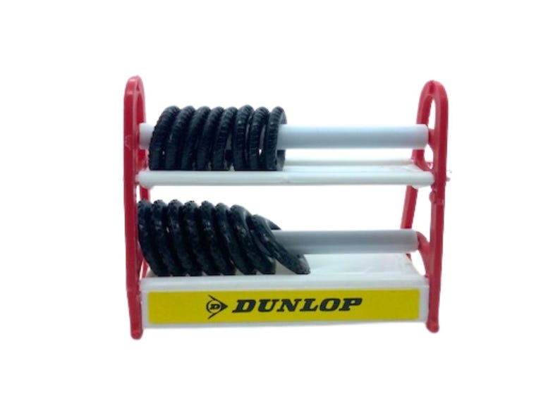 Puede incluir: Un estante rojo en miniatura para neum&aacute;ticos con dos estantes blancos que sostienen pilas de neum&aacute;ticos negros. El estante tiene una base amarilla con el logotipo de Dunlop. Los neum&aacute;ticos son peque&ntilde;os, probablemente para un coche de juguete.