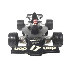 Puede incluir: Un coche de carreras de juguete negro con el número 17 y la palabra "UOP" en la parte delantera. El coche tiene la palabra "SHADOW" en el lateral y un conductor en la cabina.
