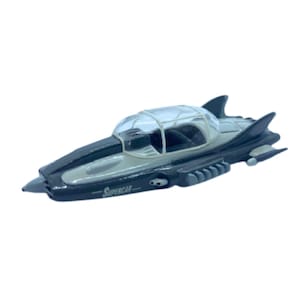 May include: A toy super car in shades of grey and black, featuring a clear bubble-shaped cockpit. The car has a sleek, aerodynamic design with fins and the word "Supercar" printed on the side. The toy is set against a white background.