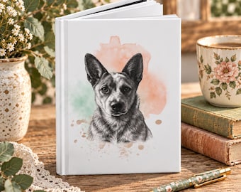 Könnte beinhalten: Ein weißes Notizbuch mit festem Einband und einer detaillierten schwarz-weißen Bleistiftzeichnung eines Australian Cattle Dog Kopfes. Der Hund ist vor einem weichen, abstrakten Aquarellfleck in Pfirsich- und Grüntönen zentriert.