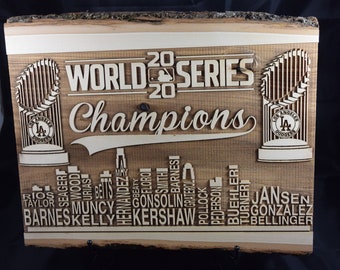May include: A wooden sign with the text "20 WORLD SERIES 20 Champions" and the Los Angeles Dodgers logo. The sign also features the names of the players on the 2020 World Series championship team.