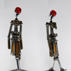 Op de afbeelding: Een serie van zeven sculpturen gemaakt van gerecycled metaal, elk met een gestileerde menselijke figuur met een rode top en een basis van tandwielen en kettingwielen.