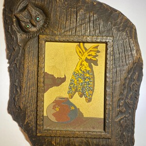 May include: A rectangular wall art piece featuring a carved dark brown wooden frame with a sculpted owl at the top left corner. The central sand art panel depicts a yellow corn cob hanging above a round, multi-colored clay pot on a tan background.