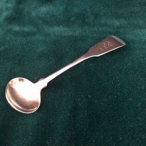 May include: A silver teaspoon with a rounded bowl and a long, slender handle. The handle is engraved with the letter "R".