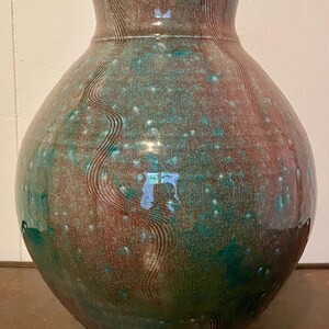 May include: A handcrafted ceramic vase with a bulbous body and a narrow neck. The vase features a mottled glaze in shades of teal, brown, and green, with a textured, wavy pattern. The vase is a decorative home decor item.