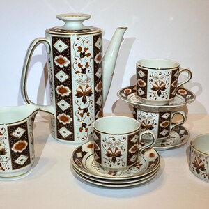 May include: A vintage tea set with a white and brown floral design. The set includes a tall coffee pot, creamer, sugar bowl, and several cups and saucers. The cups are stacked, and the set has gold trim.