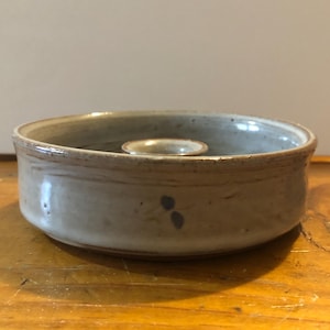 May include: A light gray ceramic candle holder with a small center ring for a candle. The holder has a subtle brown glaze and a blue floral design.