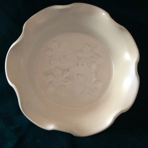 May include: A white ceramic pie plate with a scalloped edge and a floral design embossed on the bottom.
