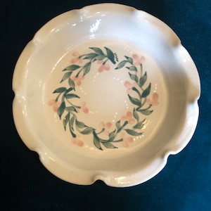 May include: A white ceramic pie plate with a scalloped edge. The plate is decorated with a green and pink floral design.