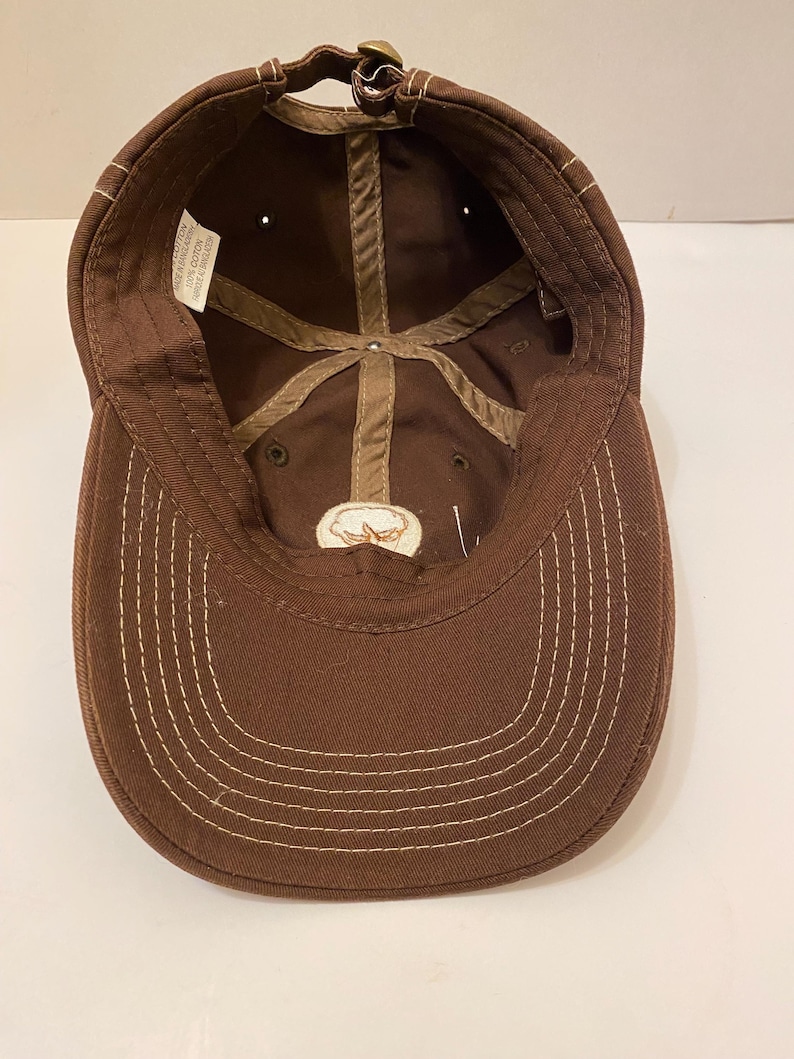 Puede incluir: Gorra de b&eacute;isbol marr&oacute;n con visera curva y correa ajustable. El interior tiene un forro de algod&oacute;n y un peque&ntilde;o emblema bordado. Las costuras blancas acent&uacute;an la visera y las costuras.