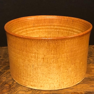 May include: A round, ceramic bowl with a light brown glaze. The bowl has a slightly textured surface and a smooth, rounded rim.