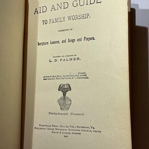 May include: Open book titled "AID AND GUIDE TO FAMILY WORSHIP." The book's contents include Scripture Lessons, Songs, and Prayers, collected by L.D. Palmer. The text also features a quote by Tennyson and the publishing information from 1923.