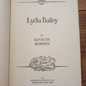 May include: A book cover with the title "Lydia Bailey" by Kenneth Roberts. The cover features a black and white illustration of a rural scene with a path, trees, and a fence.