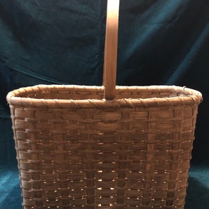 May include: A rectangular woven basket with a wooden handle. The basket is made of natural brown wicker and has a woven pattern.